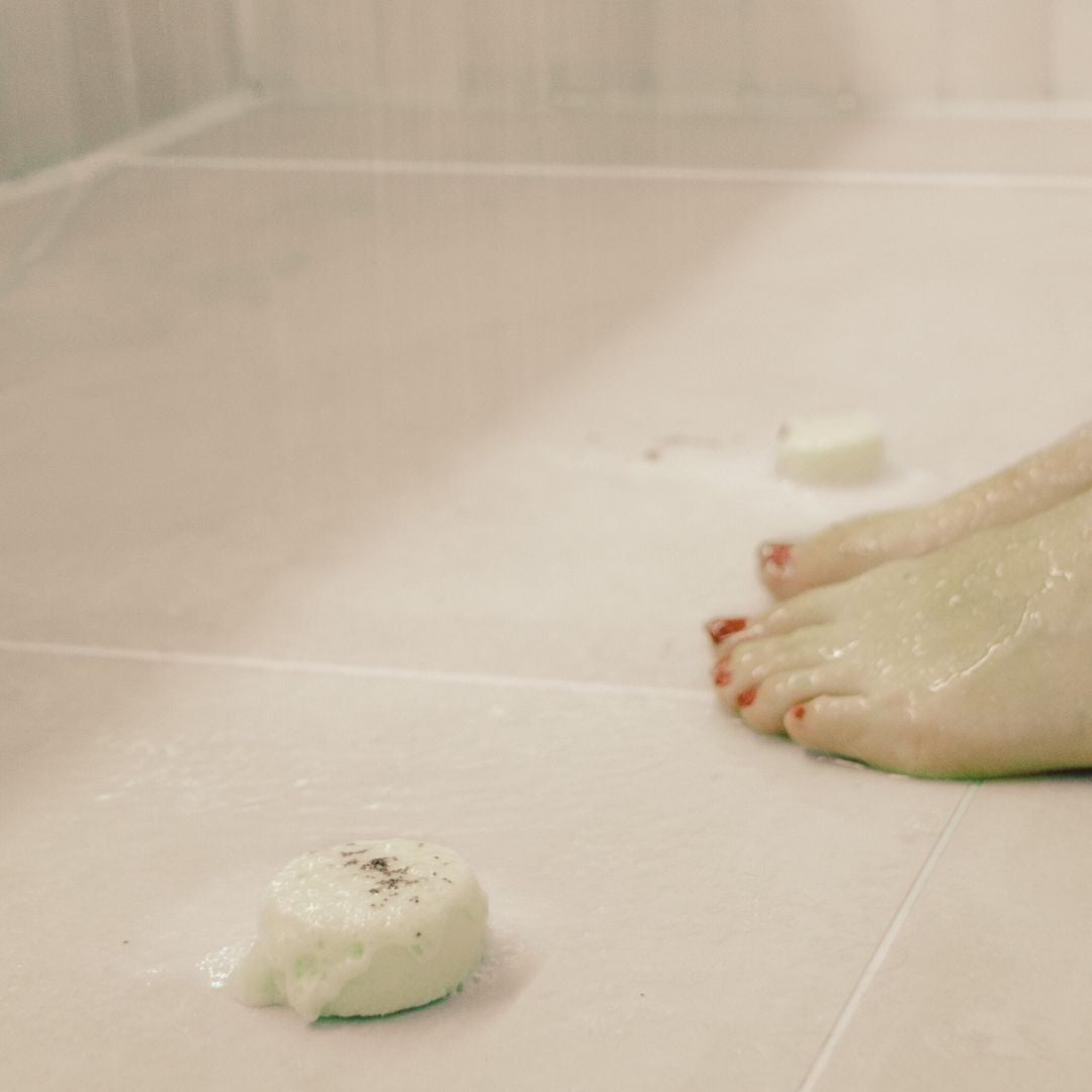 Lady using the 'Purity' shower steamer in the shower with refreshing eucalyptus, peppermint, and lemon essential oils, placed near her feet for an invigorating aromatherapy experience