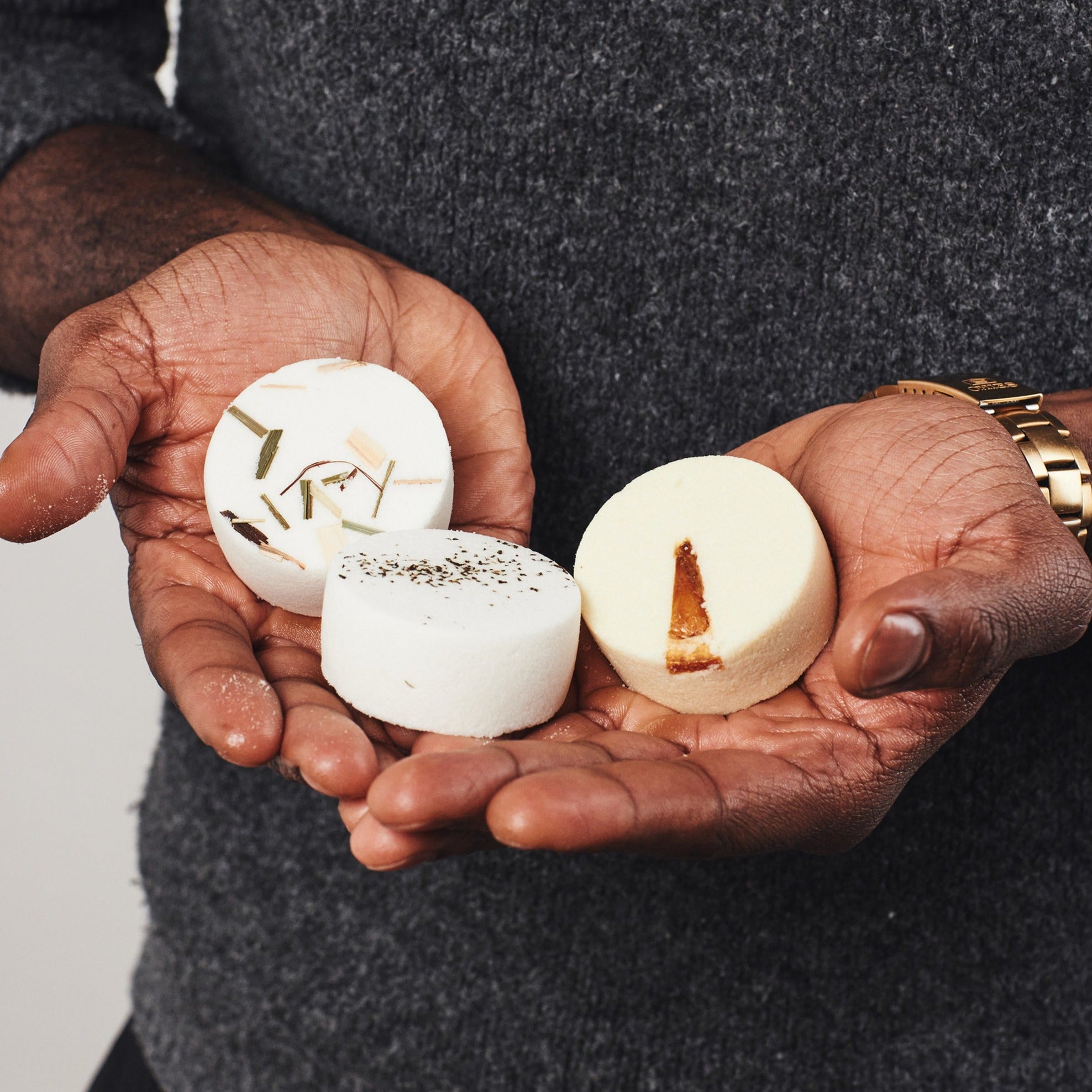 Man holding three aromatherapy shower steamers with botanicals on top: 'Clarity' (Lemongrass, Rosemary, Tea Tree), 'Vitality' (Orange, Lemon, Lime), and 'Purity' (Eucalyptus, Peppermint, Lemon).